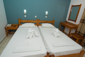 Quarto com duas camas, uma mesa de cabeceira de madeira com telefone, um banco de madeira e um espelho.