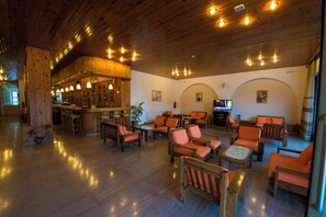 A spacious lobby with wooden flooring, a bar area, and multiple seating arrangements. - International (Kos)