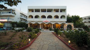 A multi-story building with a central entrance, surrounded by a landscaped garden with pathways and lighting.