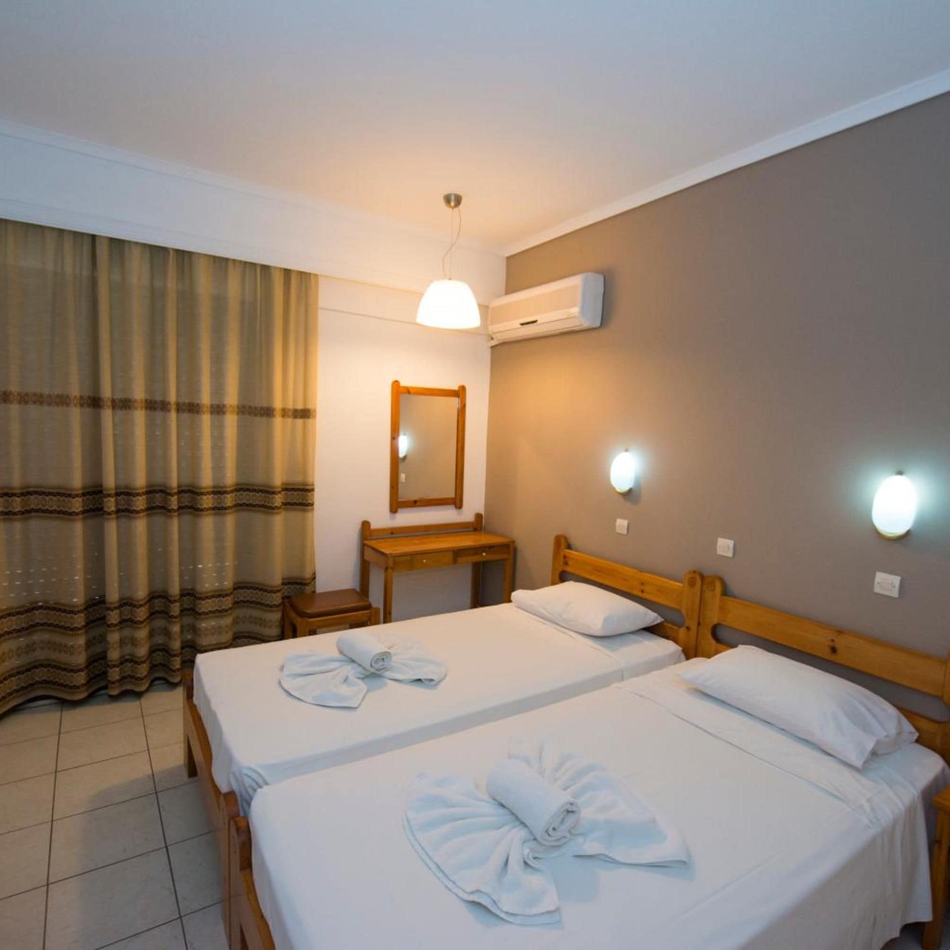 Ein Hotelzimmer mit zwei Betten, einem Spiegel, einem Schreibtisch und einer Klimaanlage.