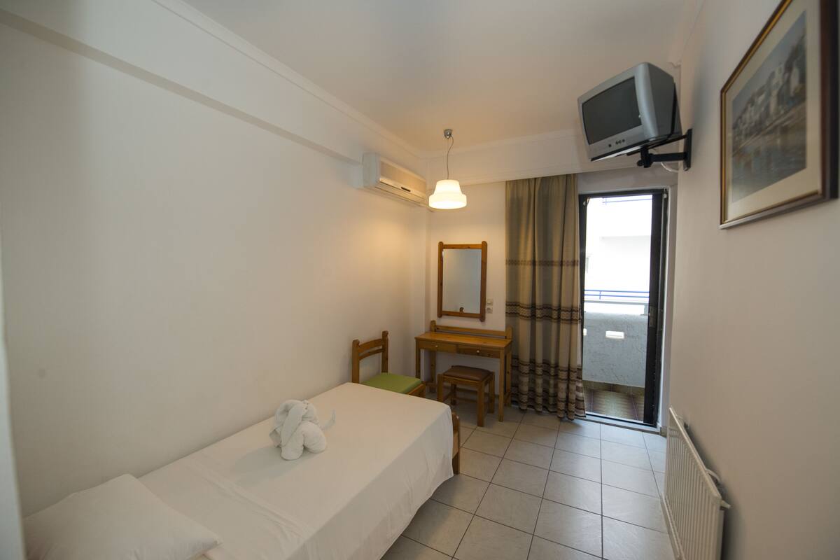 A bedroom with a bed, a desk, a chair, a television, and a window with curtains.