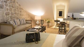 A cozy room with a stone wall, a bed with a quilt, a black quilted bag, a lamp, and a small table with a vase of flowers.