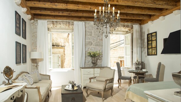 Une pièce chaleureuse avec un plafond en bois, un lustre, un canapé, un fauteuil, une table avec un vase et un lit.