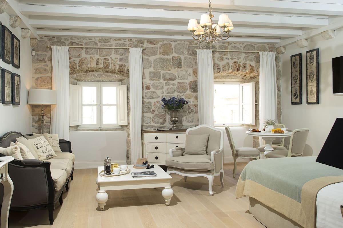 Una habitación con pared de piedra, candelabro, cama, escritorio y una silla.