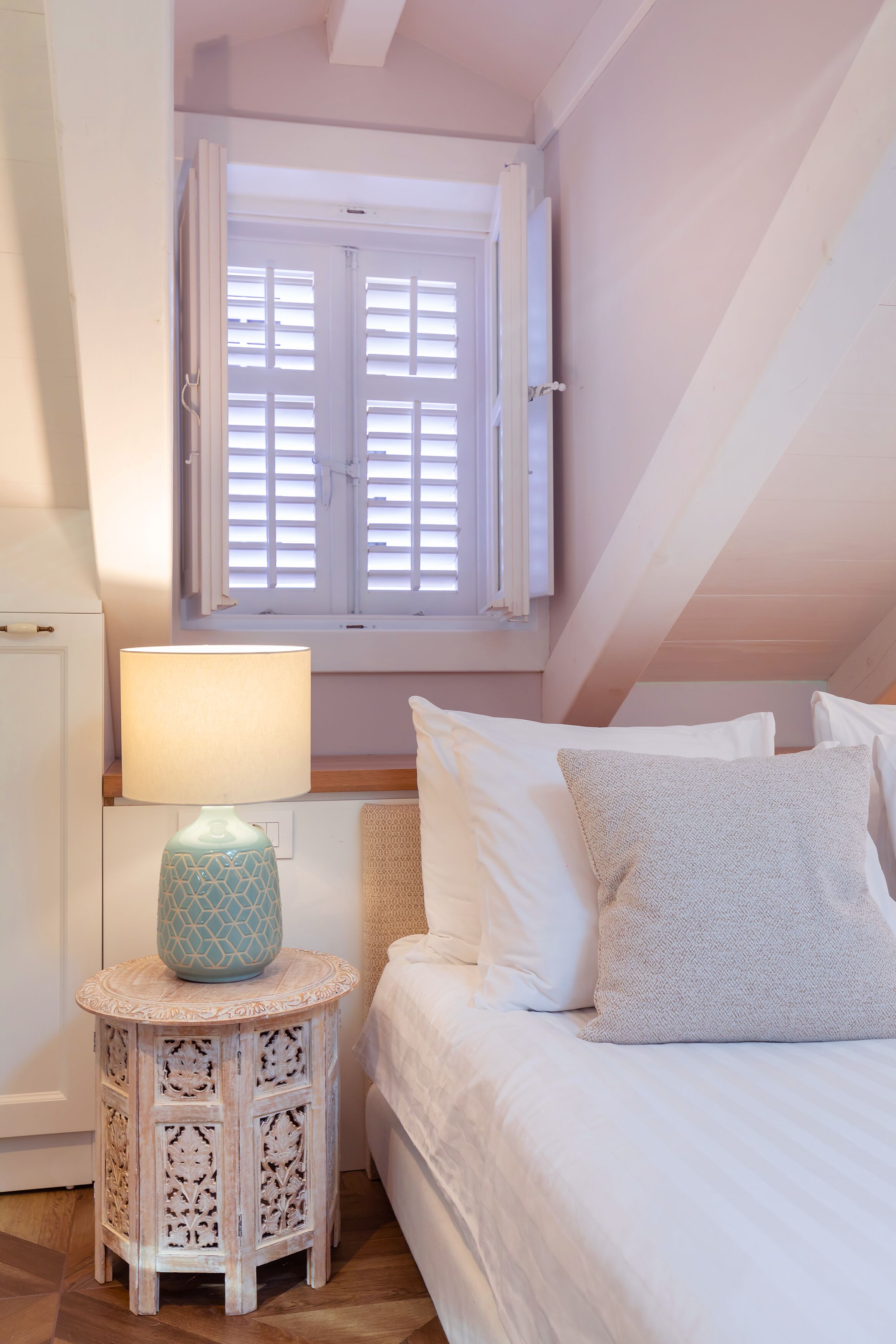 Ein Schlafzimmer mit einem Bett, einem Nachttisch mit Lampe und einem Fenster mit Rollläden.
