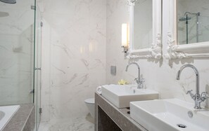 Features a sleek bathroom with a glass-enclosed shower, two sinks, and a large mirror.