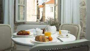 Une table de petit-déjeuner avec des croissants, des raisins, du jus d’orange et un vase rempli de fleurs.