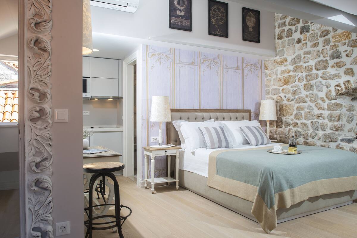 Un dormitorio con pared de piedra, cama con colcha azul y beige, dos lámparas de noche y una mesita de noche con cafetera.