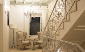 Experience the perfect blend of classic and modern style in this elegant space, featuring a grand staircase, chandelier, and plush armchairs.