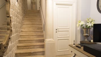 A staircase with stone steps leading to a white door, a wooden table with a vase of flowers, and a wall-mounted clock.
