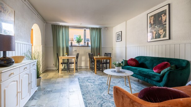 A living room with a green sofa, a wooden dining table, and a white cabinet. - Lilla Hotellet (Eskilstuna)