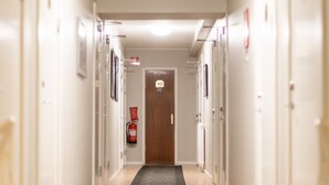 A hotel hallway with a carpeted floor, doors on both sides, and a fire extinguisher mounted on the wall. - Lilla Hotellet (Eskilstuna)
