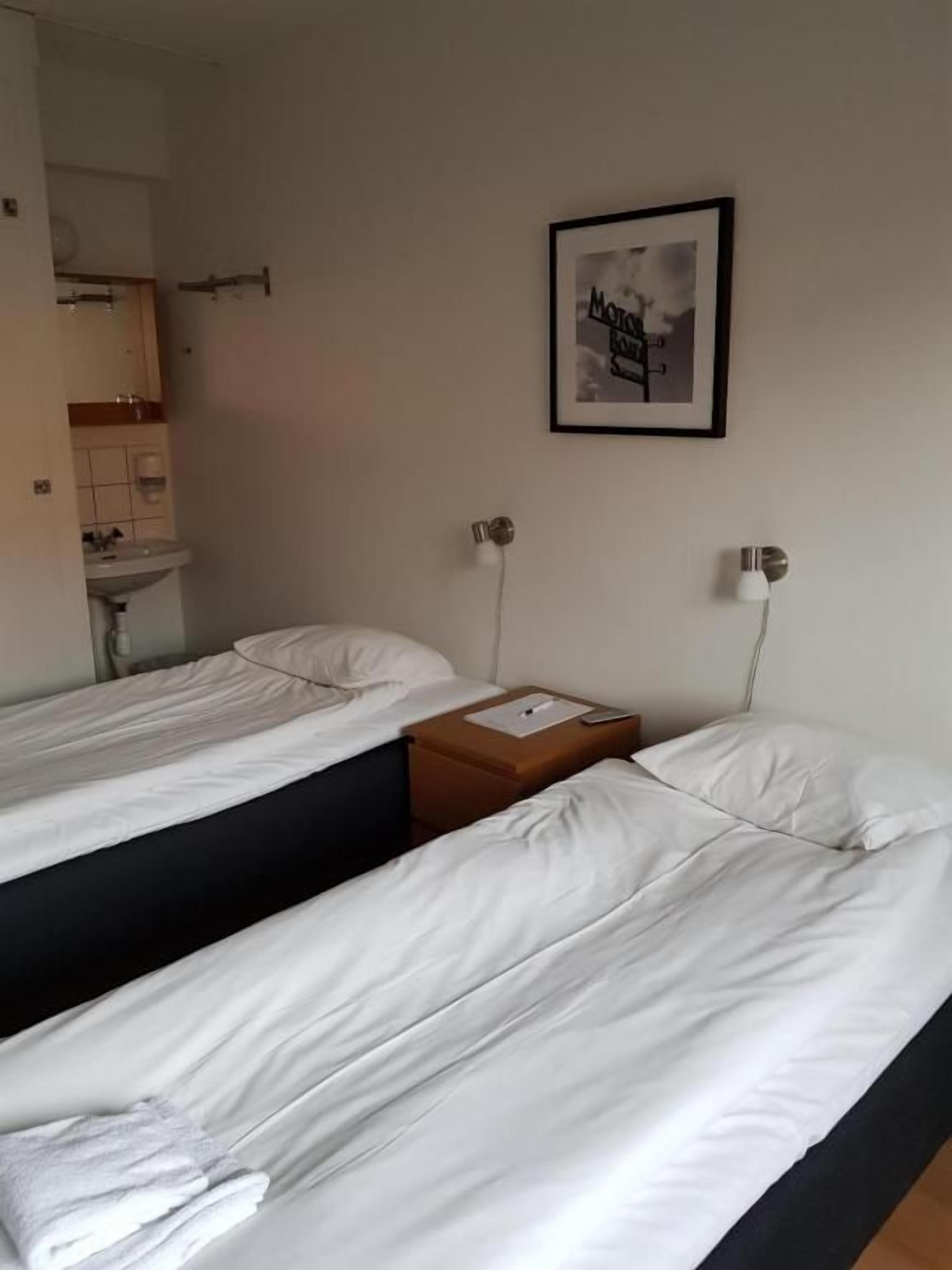 Ett hotellrum med två separata sängar, ett litet bord, en inramad tavla på väggen och ett badrum som syns genom en öppen dörr.