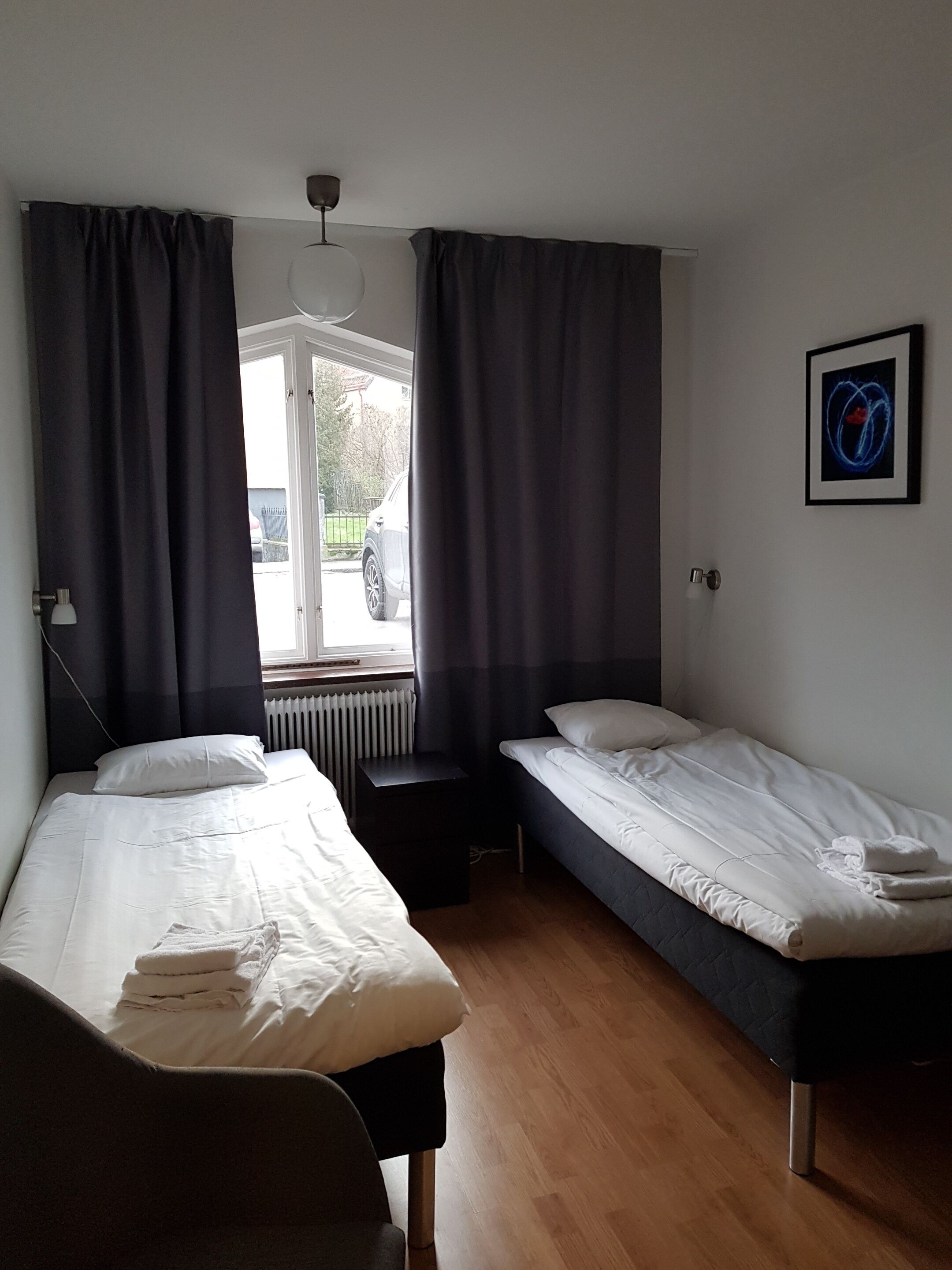 Ein Zimmer mit zwei Einzelbetten, einem kleinen Tisch, einem Heizkörper und einem Fenster mit Vorhängen.