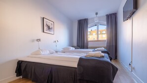 A bedroom with two beds, a window with curtains, a radiator, and a framed picture on the wall. - Lilla Hotellet (Eskilstuna)