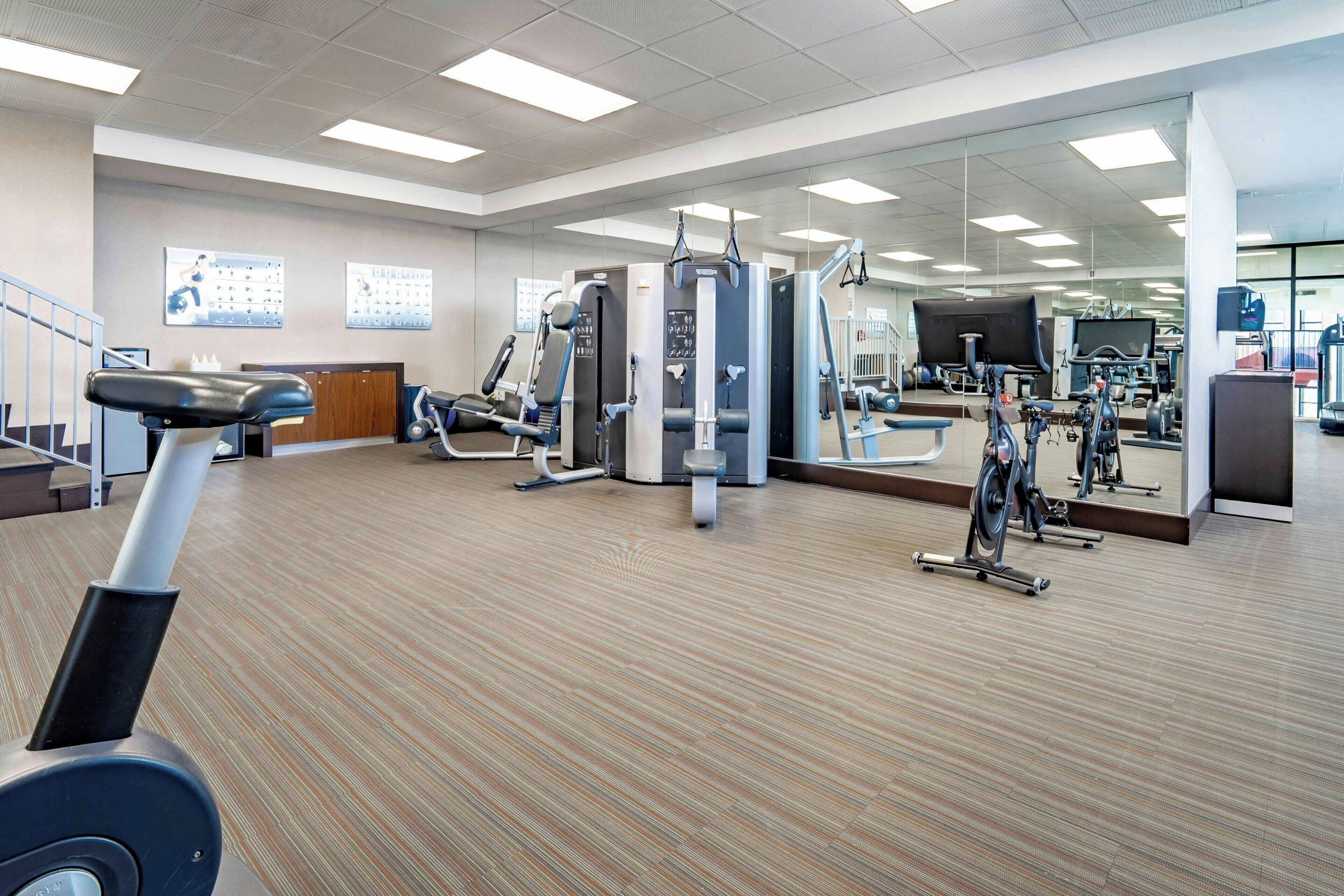 A gym with exercise equipment, a mirrored wall, and a wooden floor.
