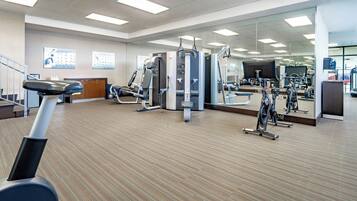 A gym with exercise equipment, a mirrored wall, and a wooden floor.