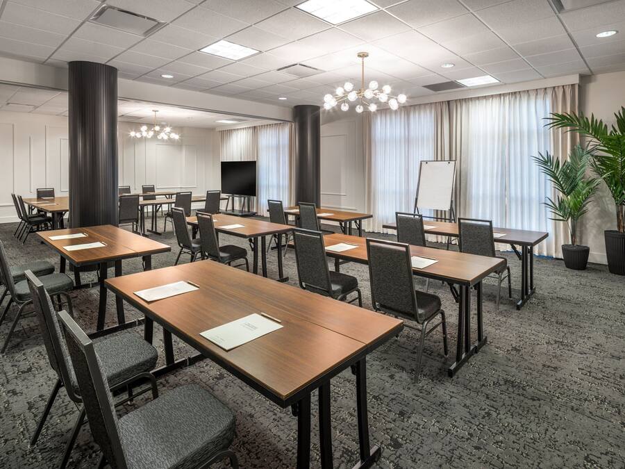 Un salón de conferencias con varias mesas y sillas, una pantalla grande y una pizarra.