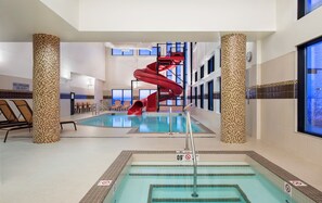 Una piscina interior con un tobogán de agua rojo, sillas de descanso y un letrero que indica que no hay salvavidas de servicio.