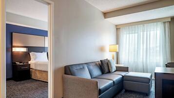 Ett hotellrum med en säng, en soffa, ett skrivbord, en lampa och ett fönster med gardiner.