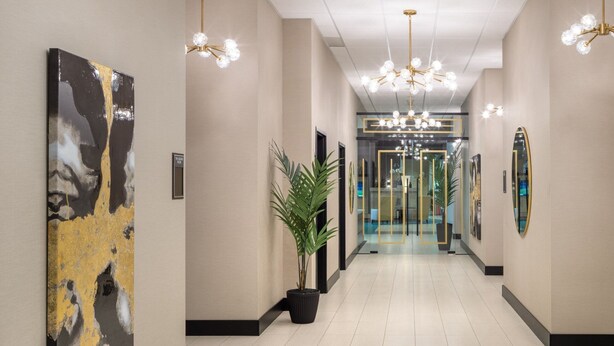 En modern hotellobby med en lång korridor, en stor abstrakt målning, en krukväxt och en entré med glasdörr.