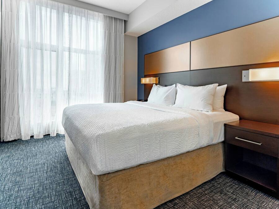 A hotel room with a bed, bedside table, lamp, and a large window with curtains.