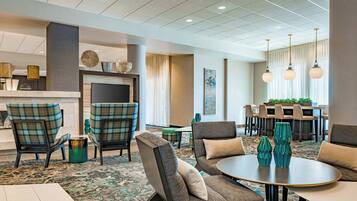 A hotel lobby with a fireplace, seating area, and a dining area.