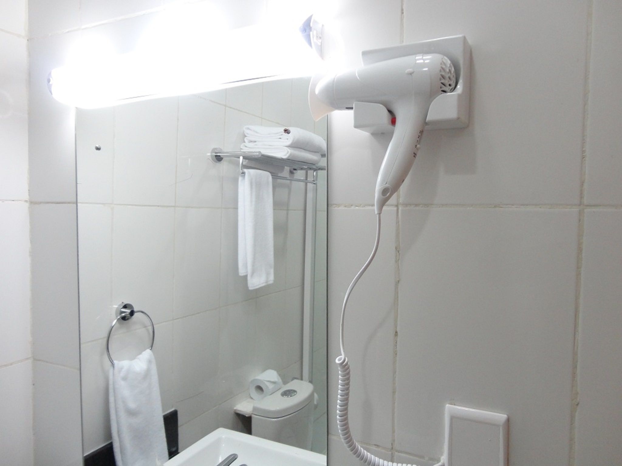 Un baño con ducha blanca, secador de pelo montado en la pared, toallero y un inodoro.