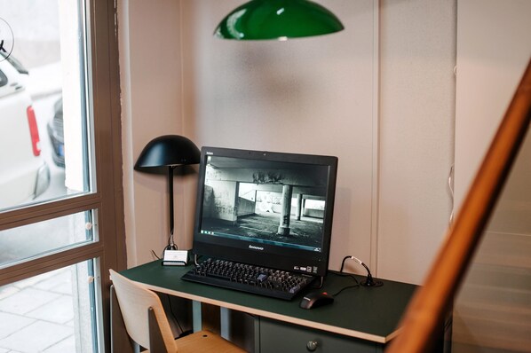 A Lenovo laptop on a desk with a green lamp, a chair, and a view of a street through a window. - Best Western and hotel (Stockholm)