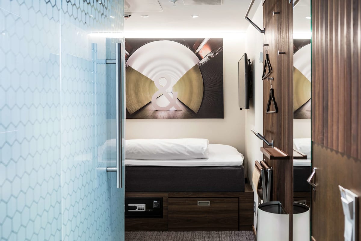 A hotel room with a bed, a desk, a mirror, and a large artwork on the wall.