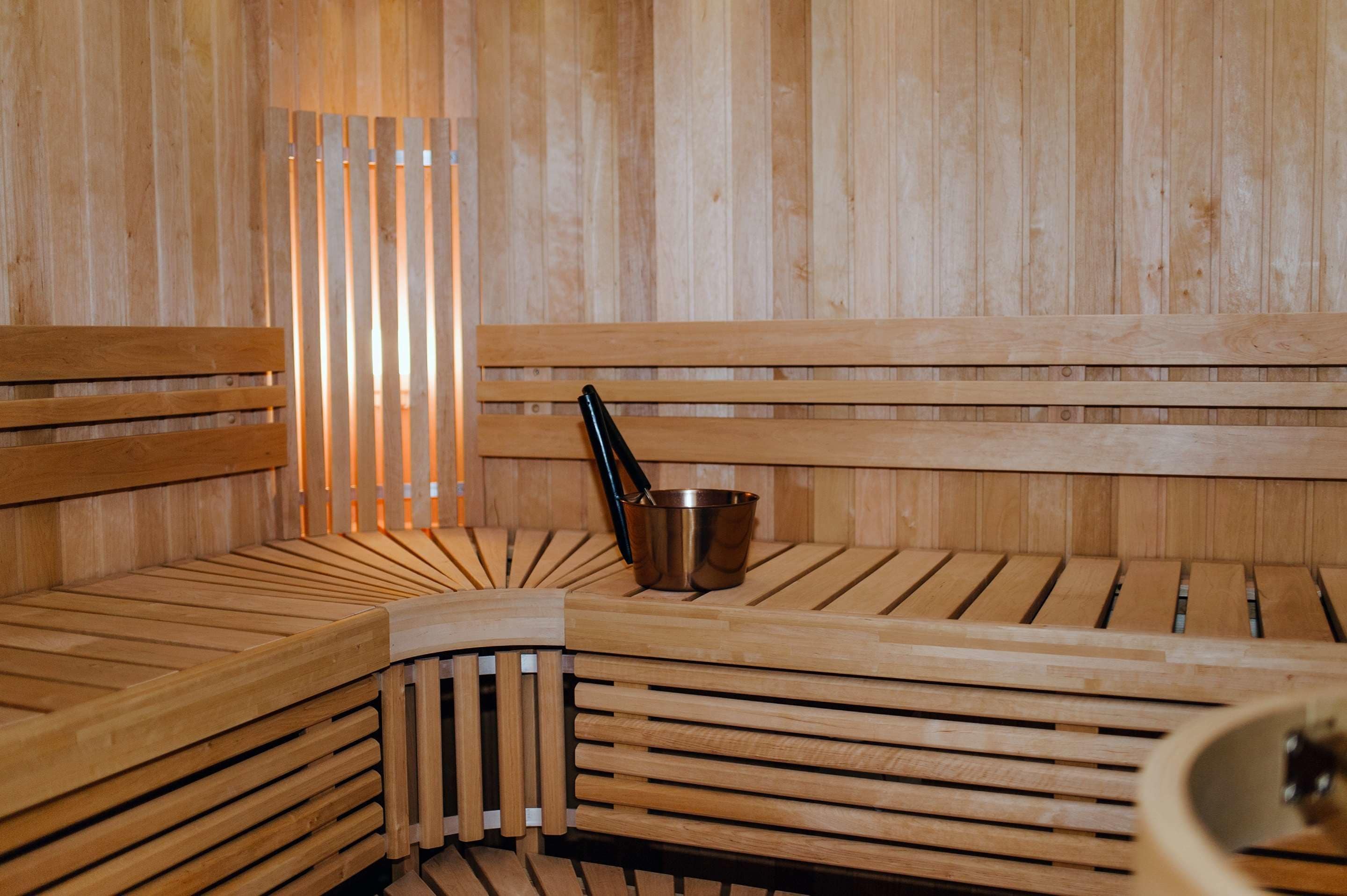 A wooden sauna with benches and a metal bucket.