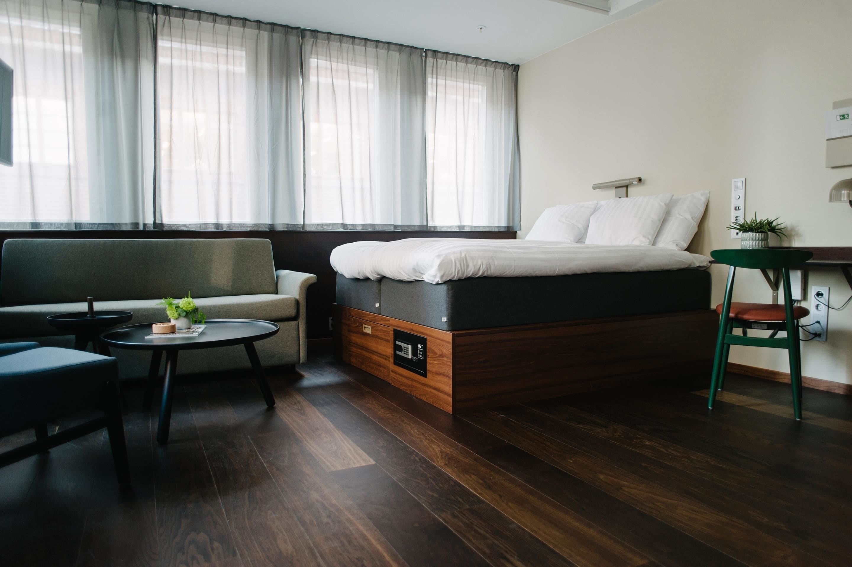 A modern hotel room with a bed, sofa, and a small table with a plant.