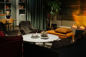 A cozy living room with a round table, a sofa, a fireplace, and a bookshelf.