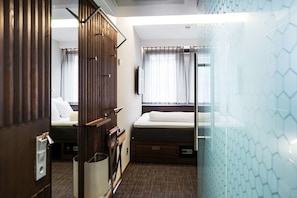 A compact hotel room with a bed, a small desk, a chair, a mirror, and a window with curtains.