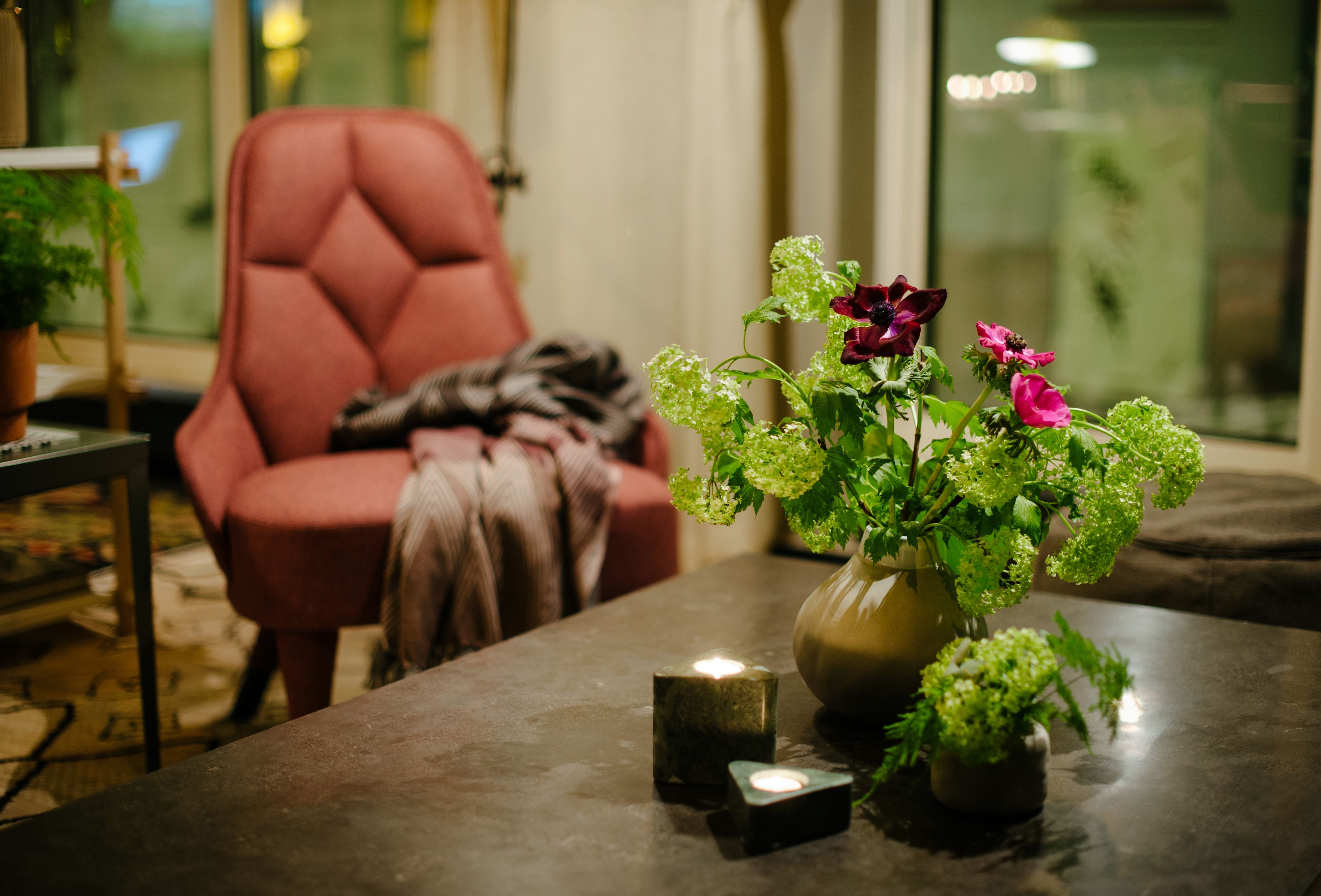 En stue med en rød stol, en vase med blomster og et lille lys på et bord.