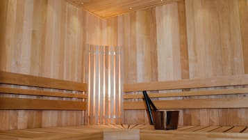 A wooden sauna with benches and a metal bucket.