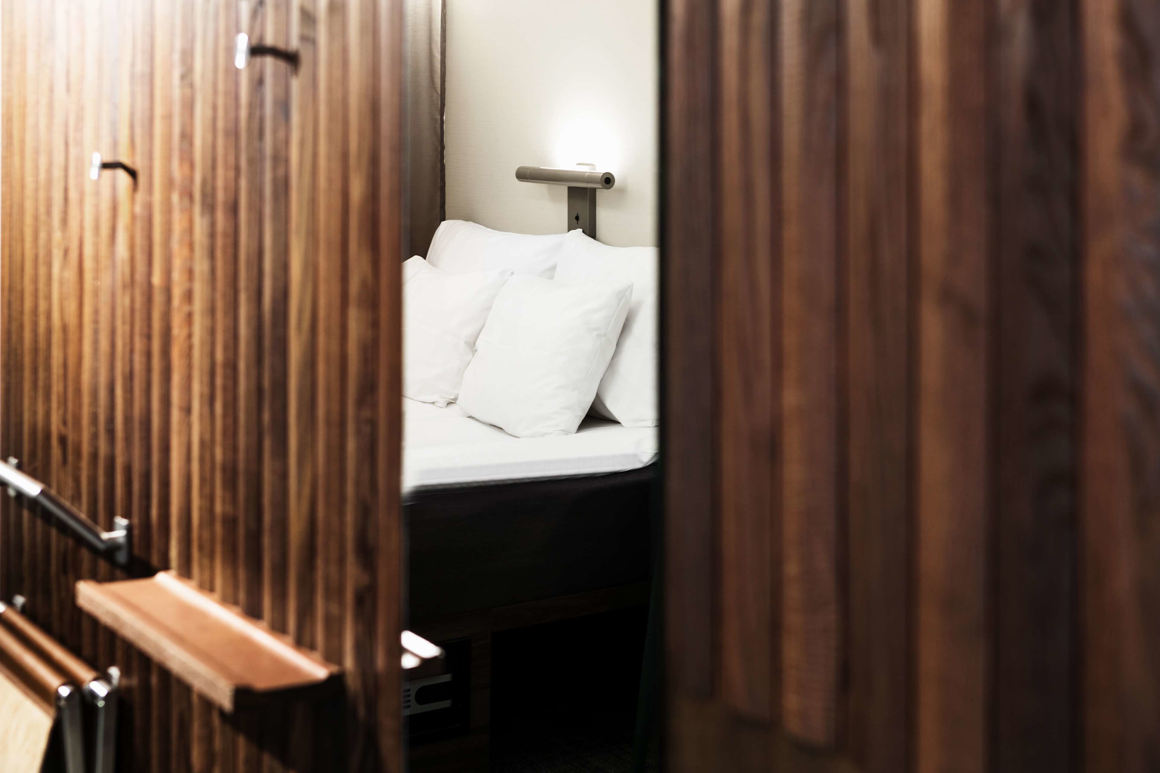 A hotel room with a wooden wardrobe, a bed with white bedding, and a nightstand with a lamp.