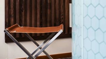 Una silla plegable de cuero marrón con patas metálicas, ubicada en una habitación con panel de madera y pared azul claro con un diseño hexagonal.