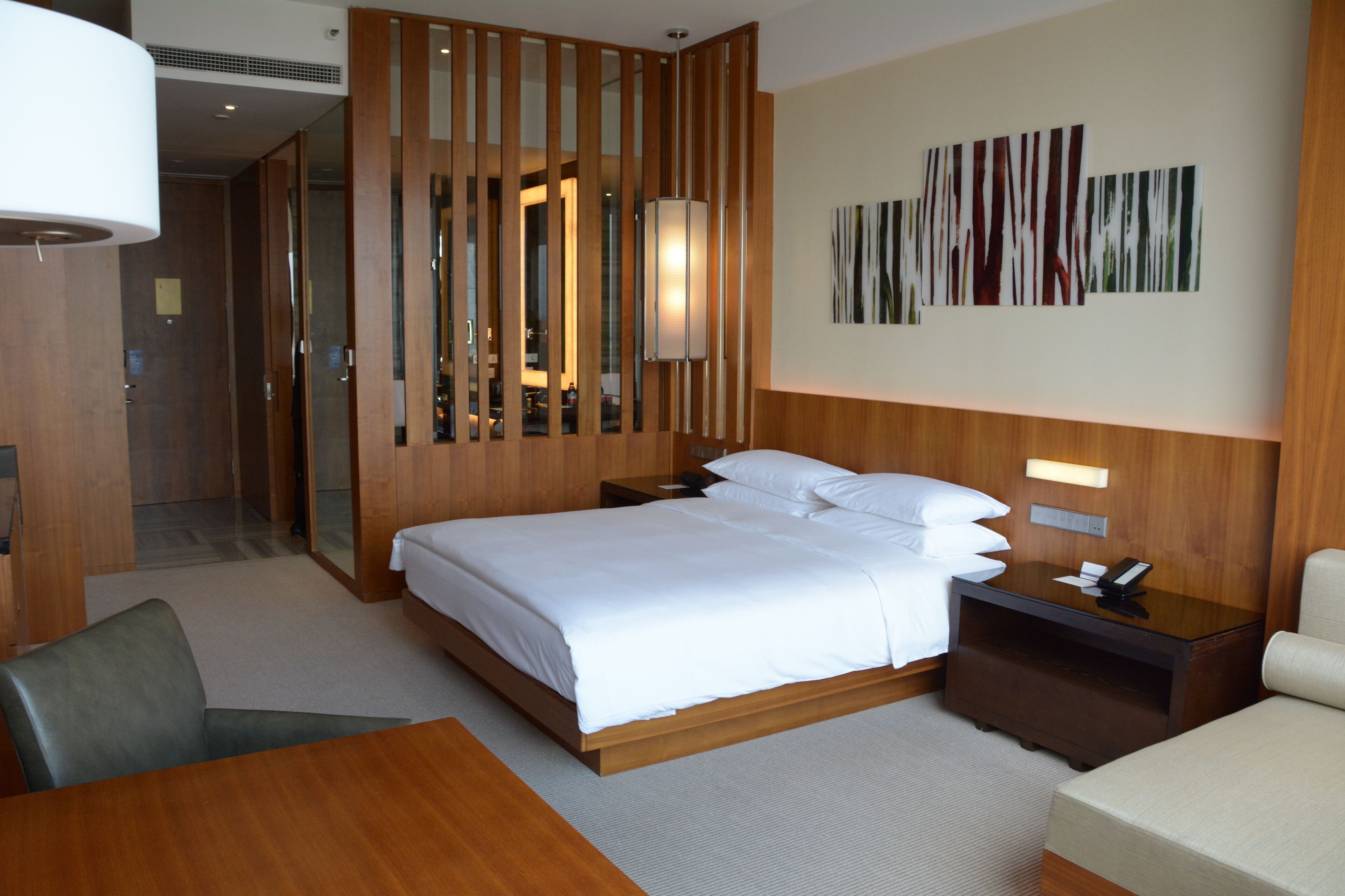 Une chambre d’hôtel moderne avec un grand lit, une cloison en bois, un bureau, une chaise et une œuvre d’art accrochée au mur.