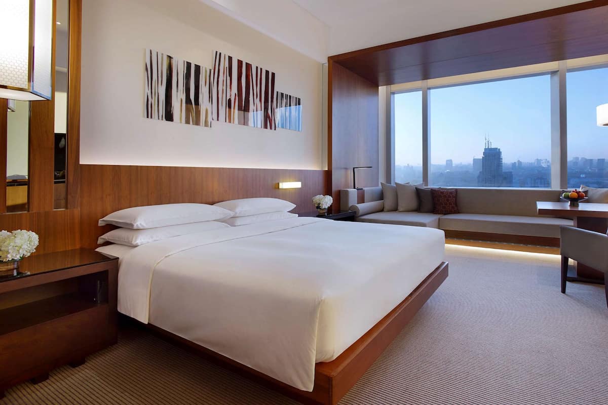 Una habitación de hotel con una cama grande, un rincón de descanso con vistas y un escritorio con lámpara.