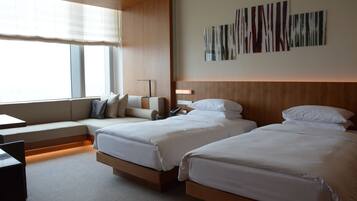 A hotel room with two beds, a sofa, a desk, and a large window with blinds.