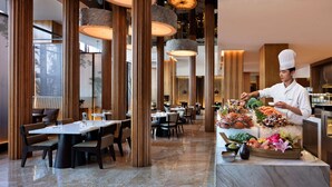 Un intérieur de restaurant moderne, avec de hautes colonnes en bois, un sol en marbre et un buffet proposant des fruits de mer et des fleurs.