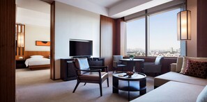 A modern hotel room with a bed, a TV, a sofa, a chair, a small table, and a large window offering a city view. - Hyatt Regency Changchun (Changchun)