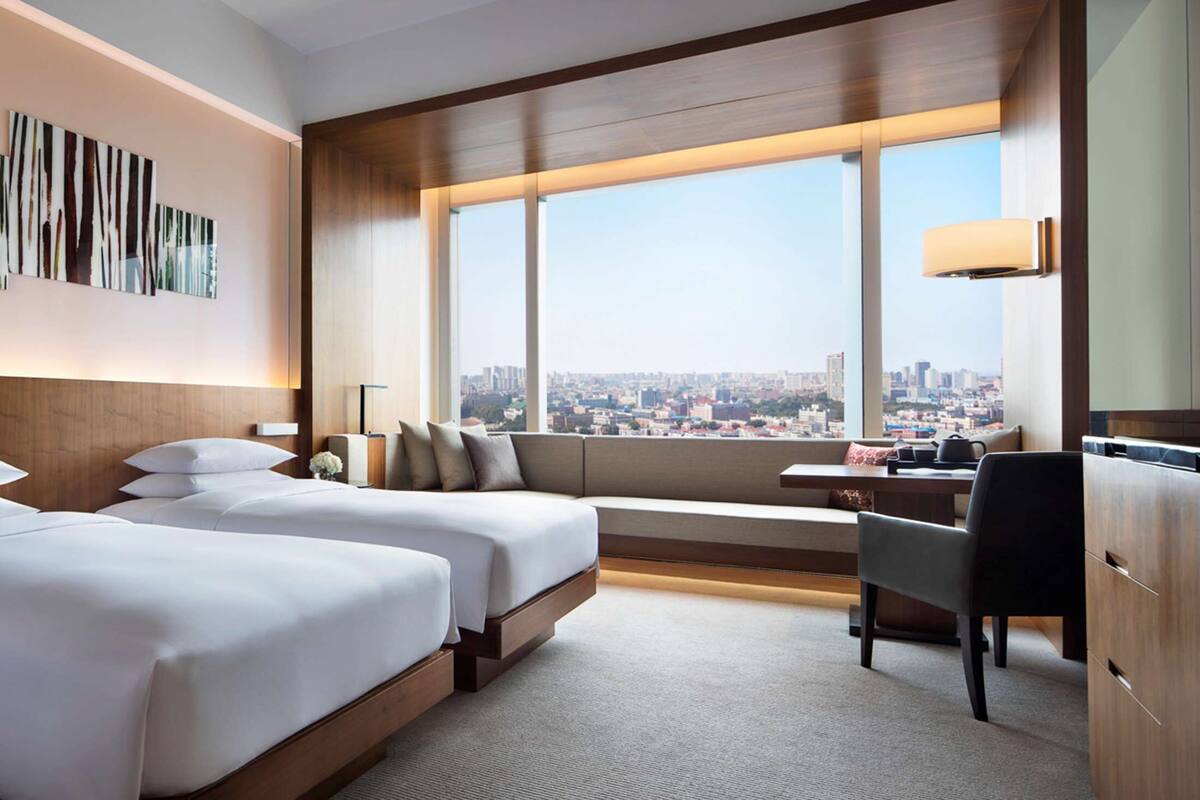 Habitación de hotel con dos camas, un escritorio, una silla, un televisor y un ventanal con vistas a la ciudad.