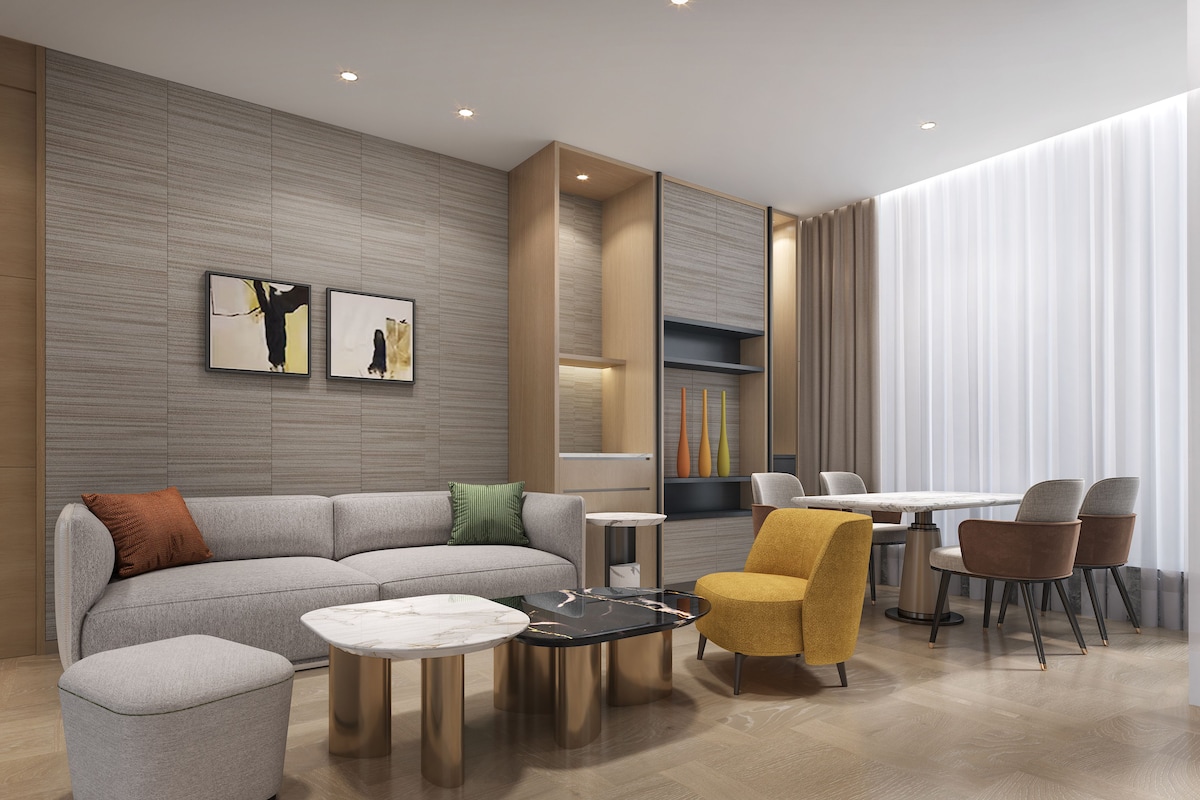 A modern living room with a sofa, coffee table, and chairs, a dining area with a table and chairs, and artwork on the walls.