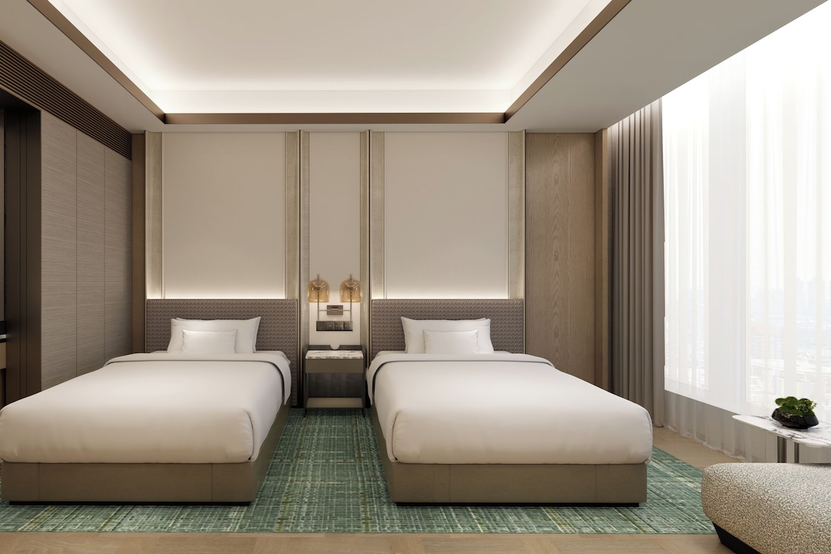 A hotel room with two beds, a large mirror, a nightstand, and a view of the city.