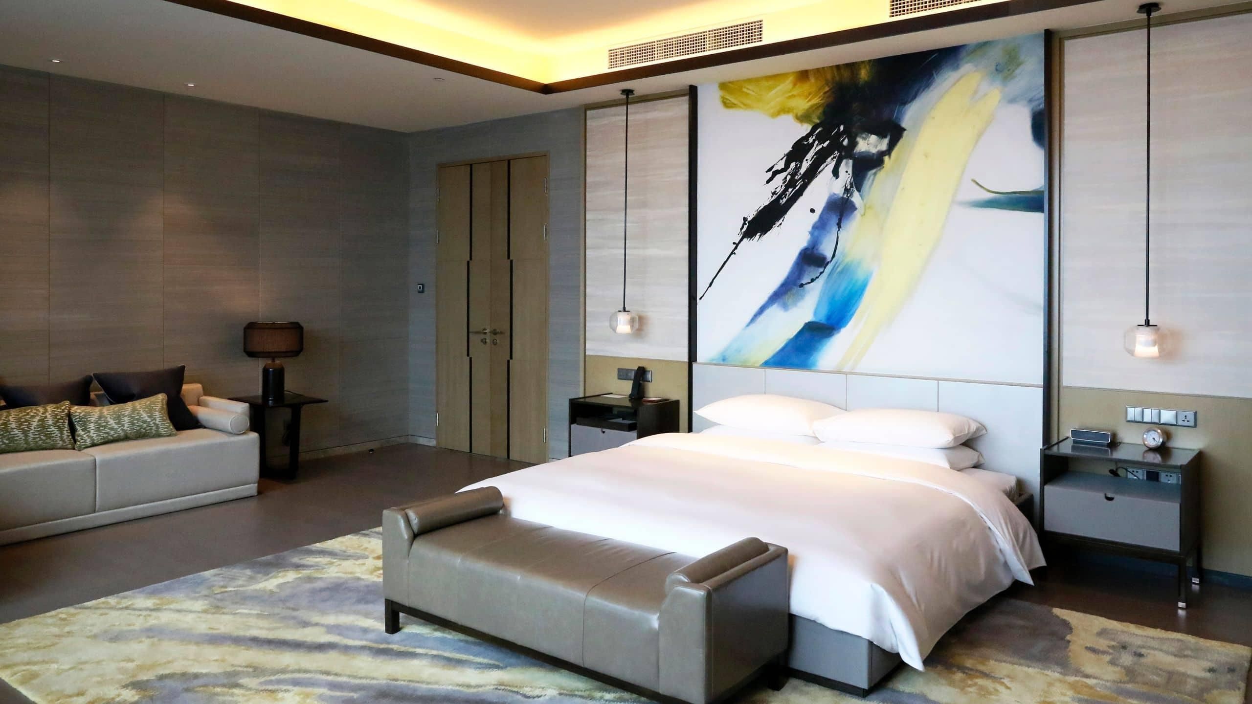 Een moderne slaapkamer met een groot bed, een bank, een bureau en een schilderij aan de muur.