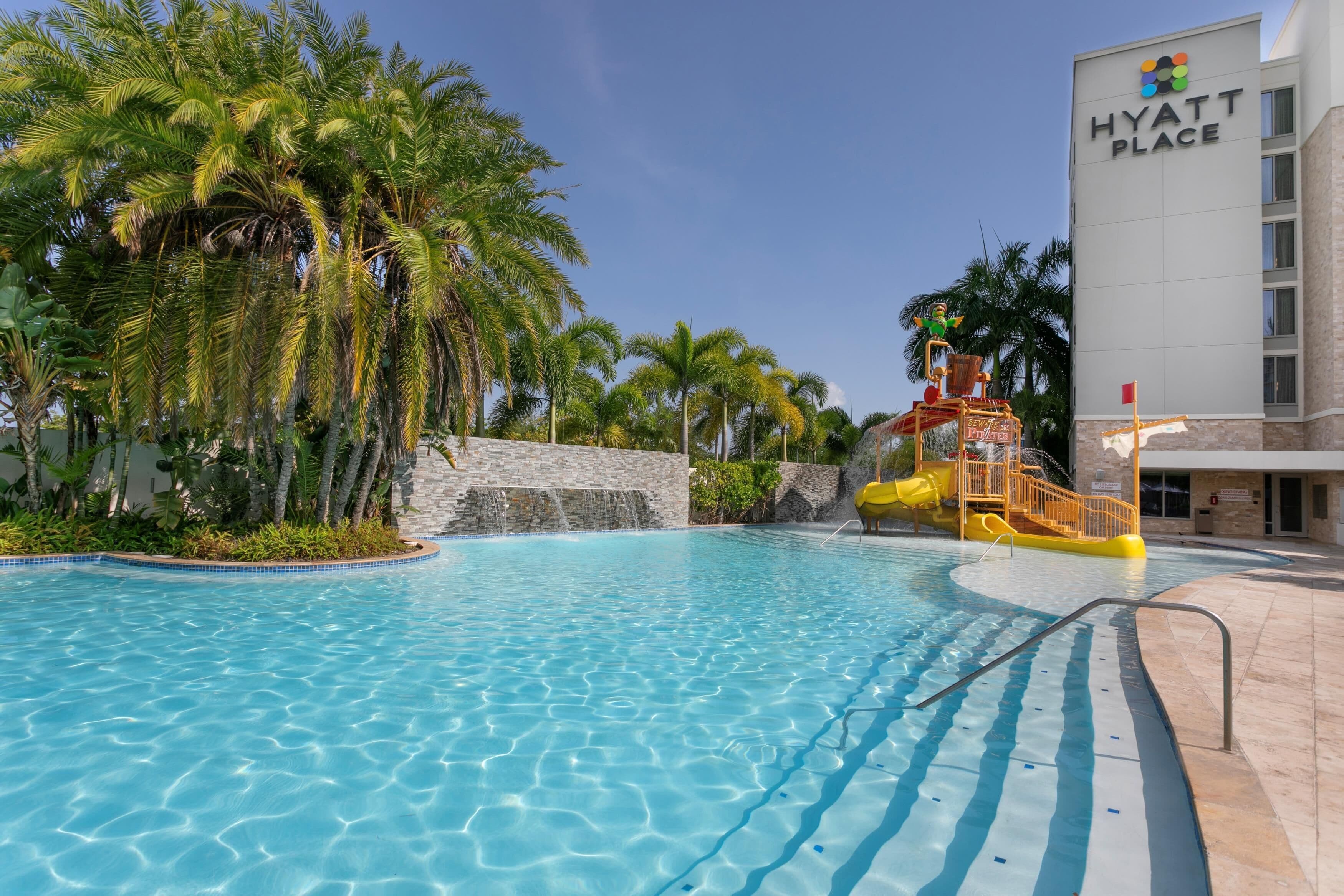 A swimming pool with a water slide, palm trees, and a building labeled 'Hyatt Place'.