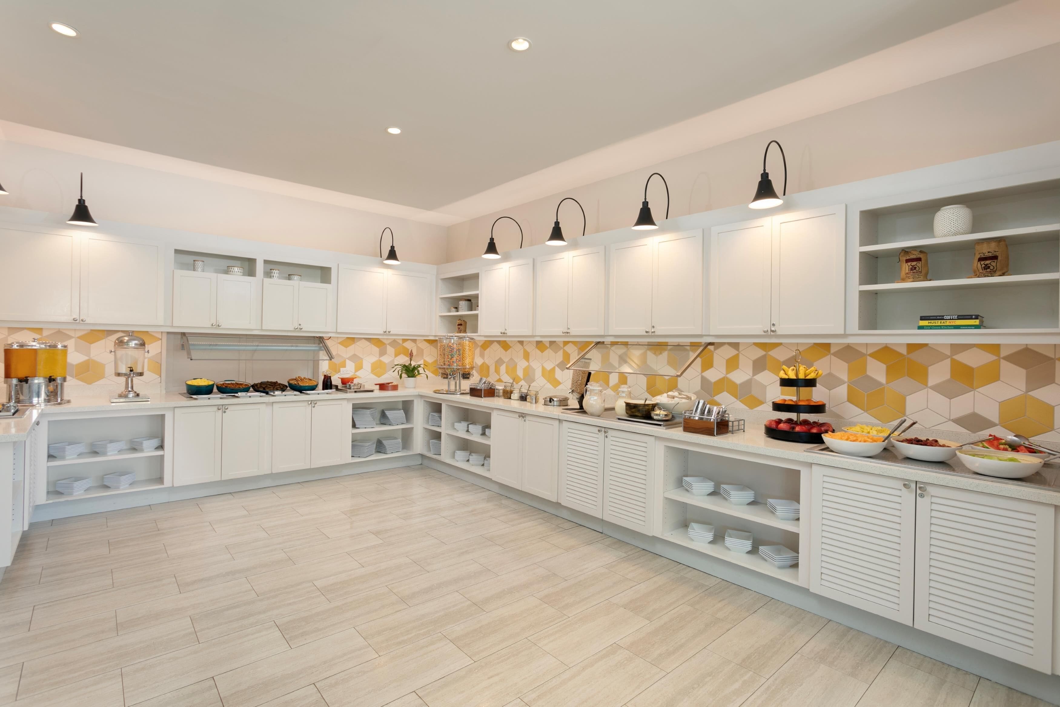 A modern kitchen with white cabinets, a herringbone-patterned backsplash, and a variety of food items on the counter.