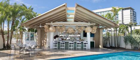 Zona de bar junto a la piscina, con piscina, asientos y barra.